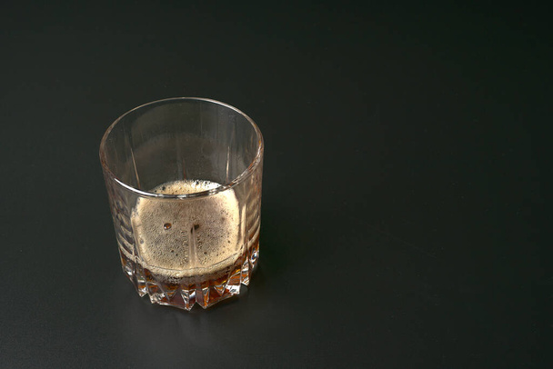 A transparent glass with fizzy soda on the bottom on a black background. - Foto, afbeelding