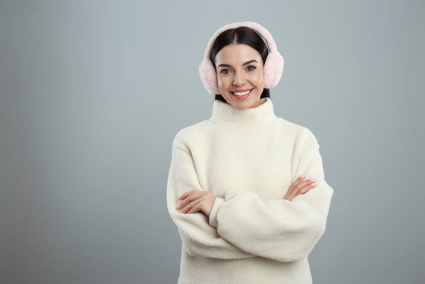 Beautiful young woman wearing earmuffs on light grey background. Space for text - Photo, Image