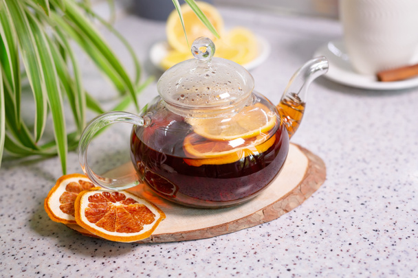 Egy forró tea ital citrommal és narancssárgával, egy teáskanna és egy fehér csésze, finom citrommal és fahéjjal. Illatos és meleg tea. 1. lépés - Fotó, kép
