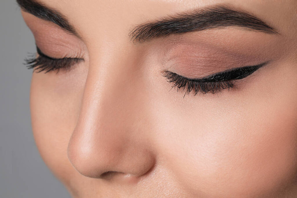 Beautiful woman with black eyeliner on grey background, closeup - Фото, изображение