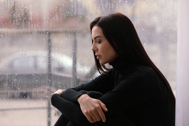 Depressed woman near window on rainy day, space for text - Φωτογραφία, εικόνα