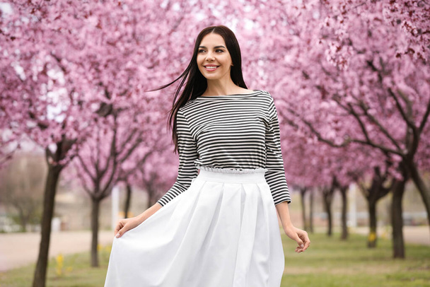Pretty young woman in park with blooming trees. Spring look - Foto, afbeelding
