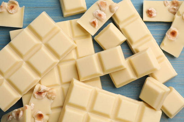 Delicious white chocolate with hazelnuts on light blue wooden table, flat lay - Zdjęcie, obraz