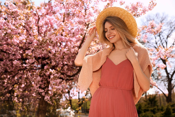 Happy stylish young woman near blossoming sakura tree outdoors. Spring look - Фото, изображение