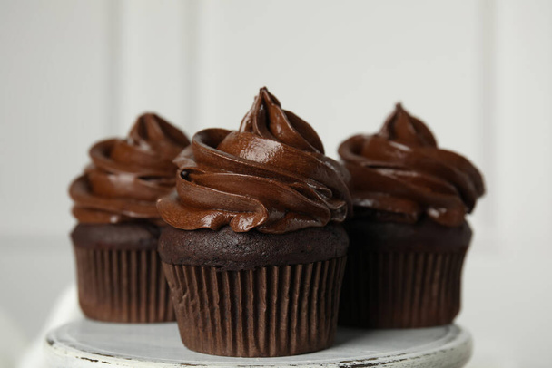 Delicious chocolate cupcakes with cream on dessert stand against light background, closeup - Photo, Image