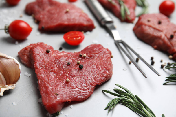 Fresh raw meat steaks and spices on light grey table, closeup - Foto, afbeelding