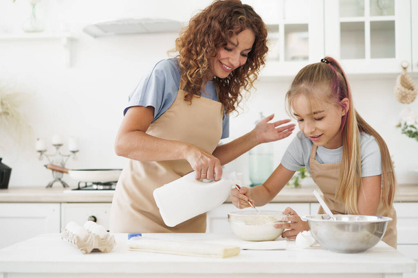 Teen girl helping her mom to cook dough in their kitchen at home - Foto, Bild
