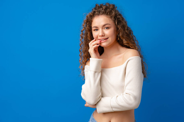 Portrait of a young attractive curly-haired woman against blue background - Fotoğraf, Görsel