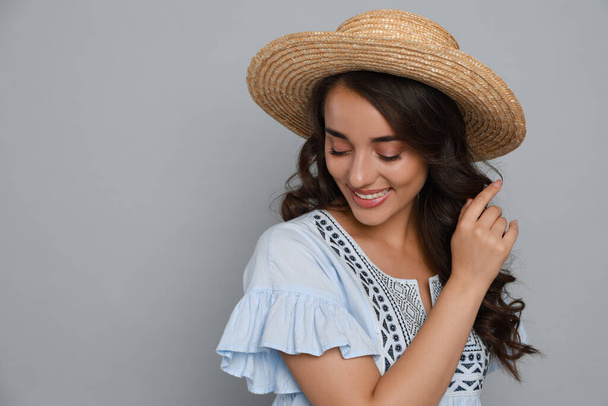 Beautiful young woman with straw hat on light grey background. Space for text - Zdjęcie, obraz