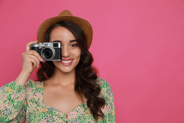 Beautiful young woman with straw hat and camera on pink background. Space for text - Zdjęcie, obraz