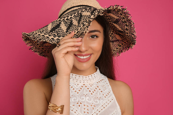 Beautiful young woman wearing straw hat on crimson background. Stylish headdress - Fotó, kép