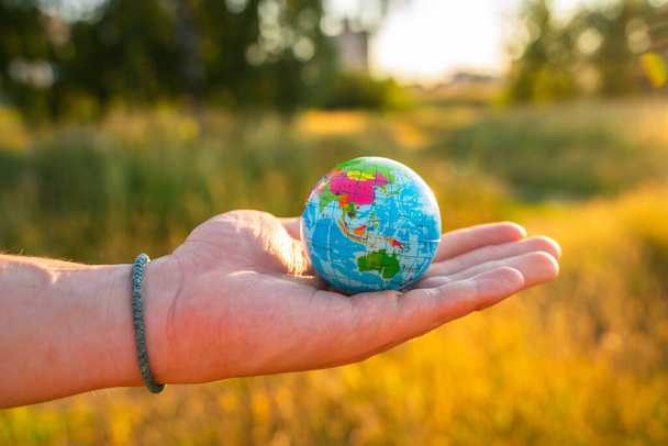 Men's hands hold a globe at sunset in the park. The concept of environmental protection - Foto, imagen