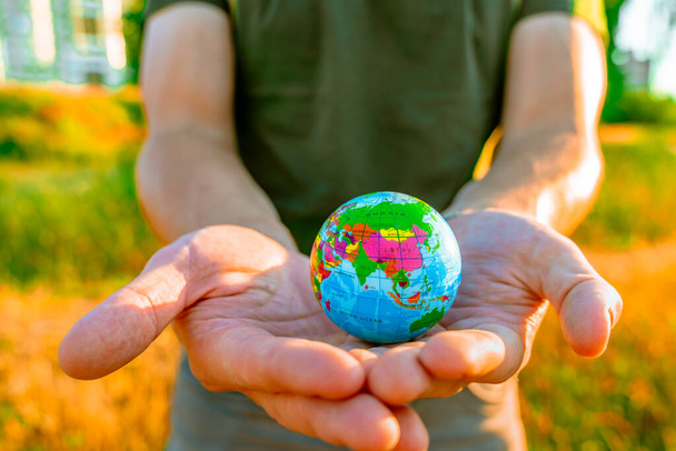 Men's hands hold a globe at sunset in the park. The concept of environmental protection - 写真・画像