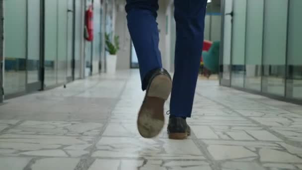 Seguimiento de piernas de hombre de negocios en traje formal caminando a lo largo del pasillo de la oficina. Pies retrovisores traseros de empresario masculino irreconocible caminando por el pasillo de oficinas de espacio abierto. - Metraje, vídeo
