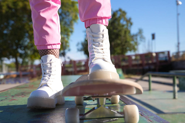 szczegóły stóp dziewczyny na deskorolce. Dziewczyna ma na sobie różowe spodnie i białe buty. Jest słoneczny dzień.. - Zdjęcie, obraz