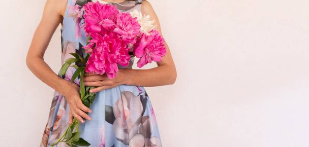 a young woman in a colorful dress with a bouquet of peony flowers in her hands on a light pink background with a copy space - Fotografie, Obrázek