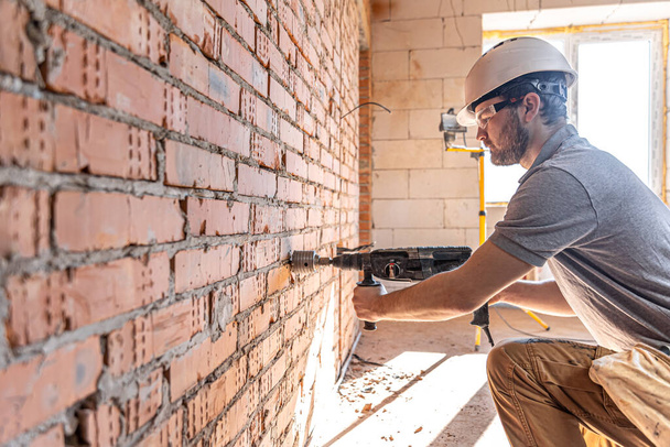 Handyman at a construction site in the process of drilling a wall with a perforator. - Foto, immagini