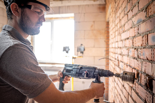 Homme à tout faire sur un chantier en train de percer un mur avec une perforatrice. - Photo, image