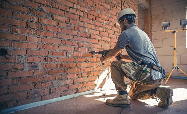 Handyman op een bouwplaats bij het boren van een muur met een perforator. - Foto, afbeelding