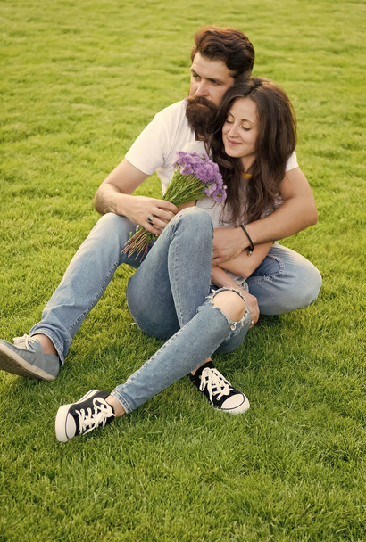 Flowers brighten day. Bearded man give flowers to sexy woman. Couple in love relax on green grass. Flower shop. Holiday celebration. Summer vacation. Flowers and natural gifts - Photo, Image