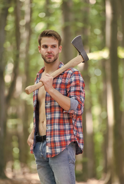 Rugged look. Unshaven man carry axe in woods. Lumberjack style. Axeman wear open plaid shirt with jeans. Casual style. Nature travel. Summer fashion. Trendy style. Everyday wardrobe - Фото, изображение