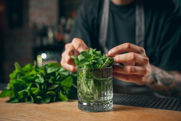 Close up image of a bunch of fresh green mint in glass standing on wooden table or bar counter. - Foto, imagen