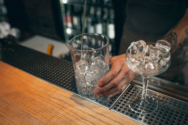 Ice in the glasses. One professional bartender mixing cocktails with long spoon in pub or cafe. Close-up image - Φωτογραφία, εικόνα