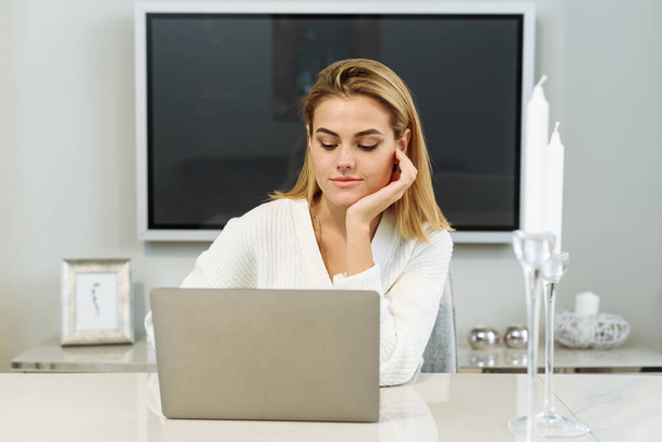 Een jonge vrouw zit thuis aan tafel en werkt in een laptop. Zakenvrouw freelancer - Foto, afbeelding