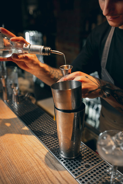 Zavřít. Jeden mladý pohledný barman připravuje alkoholický nápoj v koktejlovém koktejlu, který stojí za barem - Fotografie, Obrázek