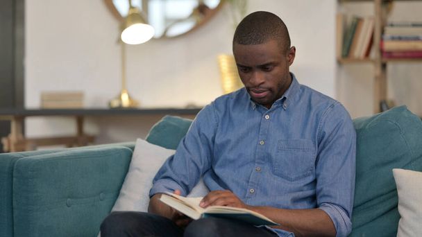 Joven africano leyendo libro sobre sofá  - Foto, imagen