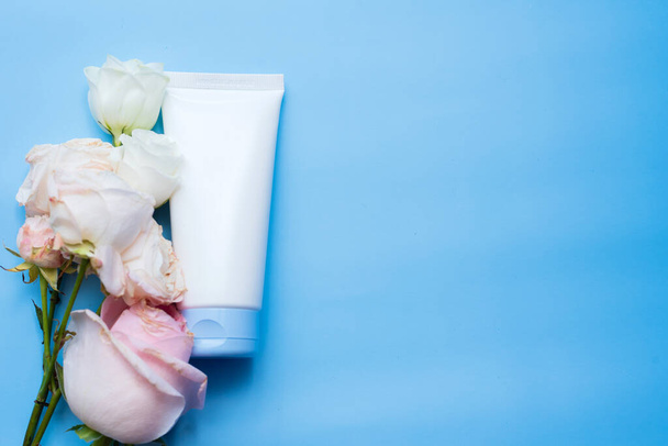 макет крема в белом пакете на синем фоне рядом с лепестками роз - Фото, изображение