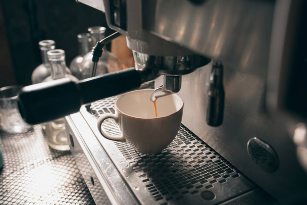 Świeża aromatyczna gorąca kawa przepływa z ekspresu do białego kubka. Zbliżenie obrazu - Zdjęcie, obraz