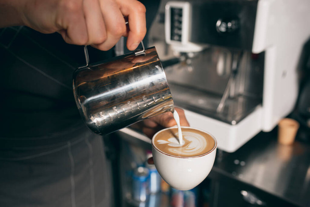 Barista giet melk in een kop koffie, zoete cappuchino of latte. Afbeelding sluiten - Foto, afbeelding