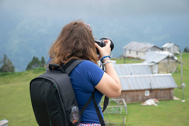 Rize, Turcja - 16 sierpnia 2017: Dziewczyna robi zdjęcia profesjonalnym aparatem fotograficznym w górach. Widok z powietrza na płaskowyż Badara i jego tradycyjne domy. - Zdjęcie, obraz