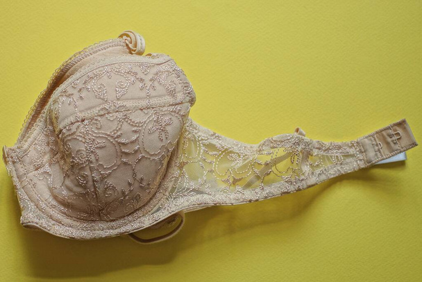 one brown empty bra made of fabric lies on a yellow table - Photo, Image