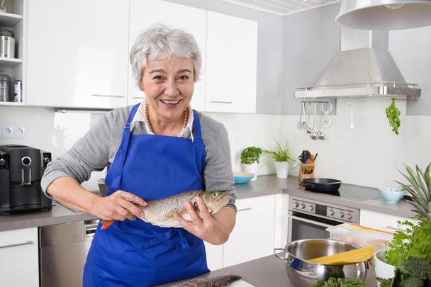 Happy senior woman in the kitchen preparing fresh fish. - Foto, imagen