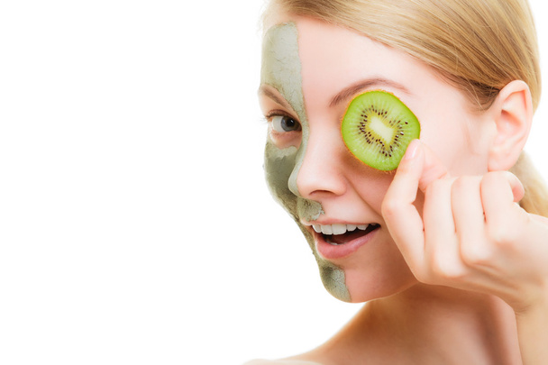Woman in clay mask on face covering eye with kiwi - Foto, Imagem