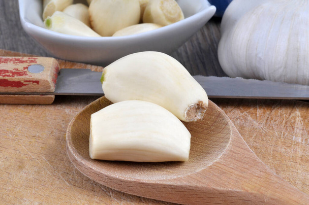 Garlic cloves in a wooden spoon next to a knife close-up  - Photo, image