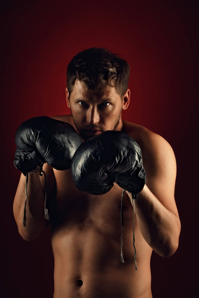 Il s'agit d'un portrait dramatique d'un boxeur en vieux gants de boxe sur un fond sombre. Un combattant athlétique des arts martiaux mixtes - Photo, image