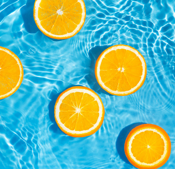 Творческая летняя композиция из нарезанного апельсина в прозрачной воде бассейна. Концепция освежения. Здоровый освежающий напиток тема. Вид сверху - Фото, изображение