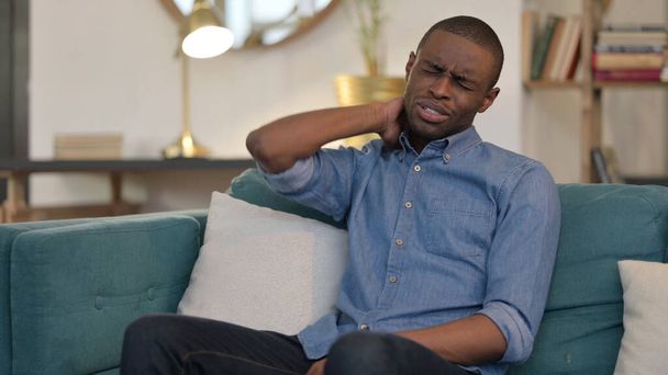 Kimerült fiatal afrikai férfi, akinek nyaki fájdalom a kanapén  - Fotó, kép