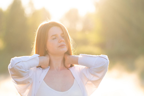 A beautiful red-haired girl in a white shirt meets the summer dawn in nature. The concept of happiness and spiritual freedom. - Foto, afbeelding
