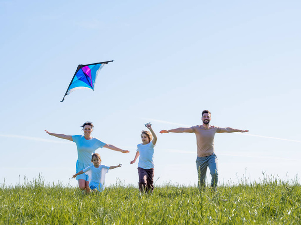 Parents and children running with kite on summer holiday vacation, perfect meadow and sky on seaside - Photo, Image