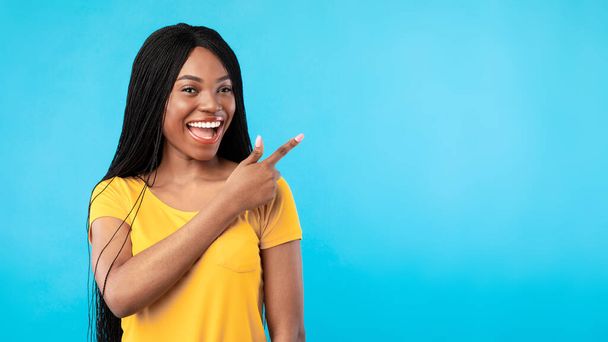 Negro femenino señalando dedo aparte mostrando Copyspace, fondo azul - Foto, Imagen