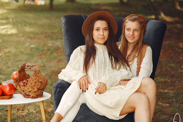 Elegant and stylish girls sitting on a chair in a autumn park - 写真・画像
