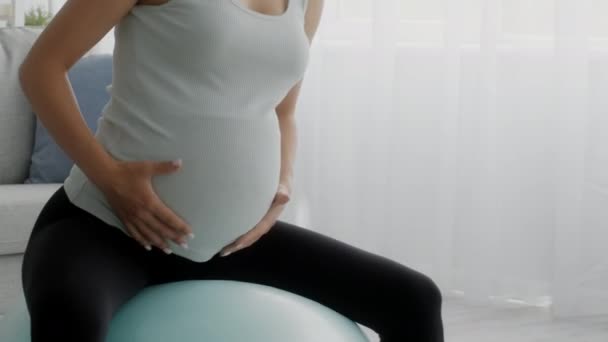 Zwangere vrouw doet oefeningen op fitness bal thuis, close-up schot - Video