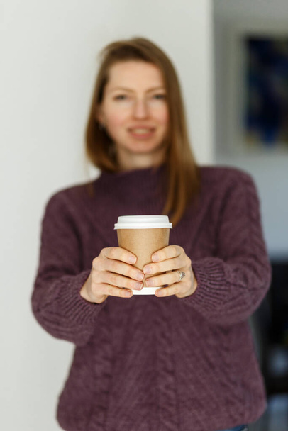 Soft focus pretty young woman in stylish violet sweater holding cup in hands. Warm soft cozy image. Details. Drinking take away coffee. Breakfast on the go. Instagram style toned image. Focus on cup - Foto, imagen
