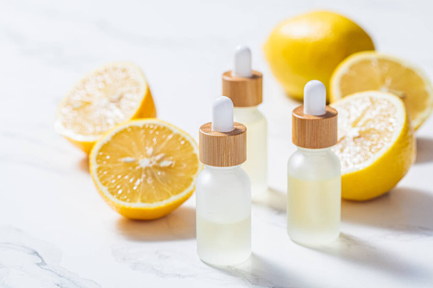 Lemon essential oil in glass bottles, white marble background. Skin and body care concept. - Zdjęcie, obraz