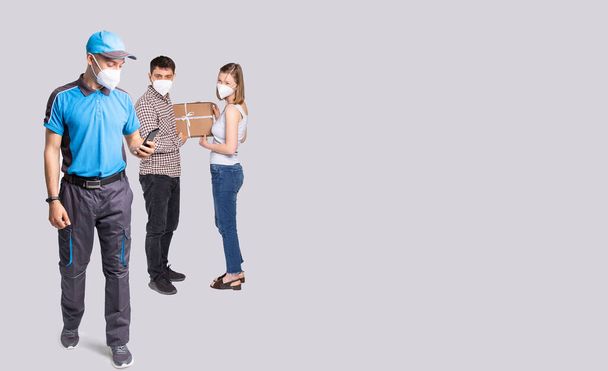 Courier with the mobile phone in the hand delivered a box during a pandemic time so they are wearing a mask.  - Foto, imagen