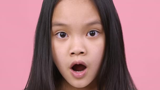 Szokujące uczucie. niesamowite mała dziewczynka patrząc na aparat z otwartymi ustami, uczucie szoku i zdumienie, różowe tło - Materiał filmowy, wideo